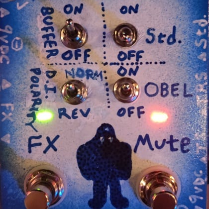 front panel of a hand-made pedal with four toggles, two footswitches, a green LED, and a red LED. there is a sketch of a golem character in the middle